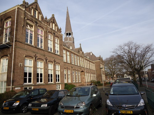 Baanstraat 72  6 januari 2015
De Bisschoppelijke Kweekschool gelegen aan de Baanstraat dateert uit 1906. De bisschop van Haarlem nam reeds in 1869 het initiatief tot oprichting van de Vereniging tot bevordering van het katholiek bijzonder onderwijs. Echter pas in 1897 werd een eigen school opgericht, een kweekschool dus, eerst in Hoorn, maar in 1906 werd de school naar Beverwijk verplaatst. Een nieuw gebouw werd gesticht op grond aangekocht van de familie Waterschoot van der Gracht. De school werd ontworpen door architect J.J.L.Moolenschot. Bij de Kweekschool werd ook de R.K.Leerschool gebouwd, daar konden de kwekelingen praktijk opdoen. Aan de Romerkerkweg en de Kees Delfsweg werden enkele burgerwoonhuizen gebouwd, daar kwamen uiteraard R.K. ingezetenen te wonen die zorgden voor het huisvesten van de kwekelingen, kosthuizen dus. In 1922 werd bij de kweekschool het internaat gebouwd, dat was nodig omdat de kwekelingen ontevreden waren over huisvesting en eten en drinken terwijl de kostbazen vonden dat zij te weinig vergoeding kregen. Het voert te ver de gehele geschiedenis van de Bisschoppelijk Kweekschool hier weer te geven. De school veranderde van naam en werd in later jaren Katholieke Pedagogische Academie Beverwijk. Problemen op velerlei terrein ontstonden er in 1969, er volgde bezetting van de school door de leerlingen, daarna een ontruiming en eigenlijk is het nooit meer goed gekomen. Het leerlingenaantal daalde drastisch, er kwam een samenwerking tot stand met de Opleiding voor het kleuteronderwijs in Bergen en een fusie volgde per 1 januari 1982. De school vertrok naar Bergen, naar de Katholieke PABO. De school werd verbouwd, er kwamen 55 wooneenheden in en het appartementencomplex werd in 1989 weer in gebruik genomen. 

Foto’s : Prentenkabinet van der Linden/Co Backer
Tekst: Co Backer
Keywords: Bwijk Baanstraat
